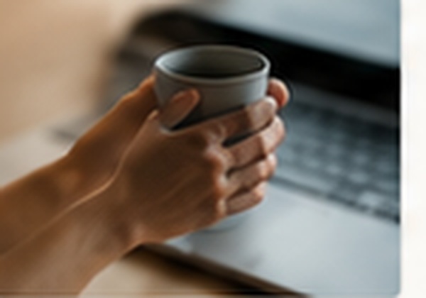 A hand holding coffee beside a laptop
